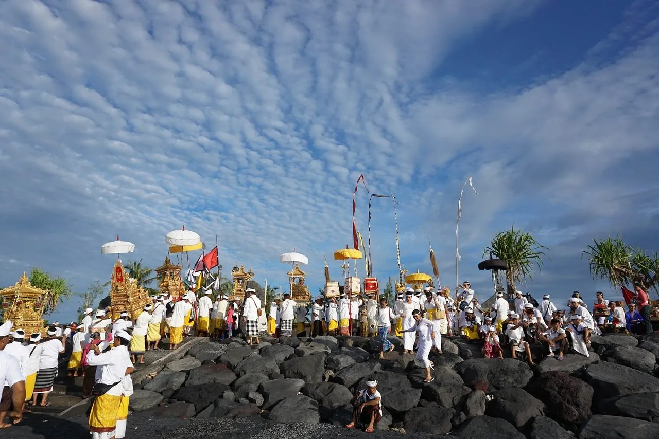 Image of Hindu devotees on dark grey rocks with white cloud streams in the sky.