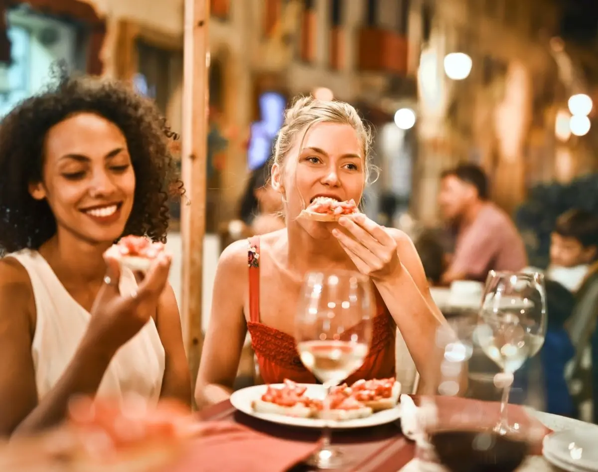 Two women eating pizza and drinking wine in a busy restaurant