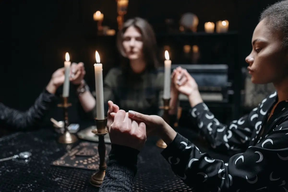 Women holding seance in a dark room holding hands around table